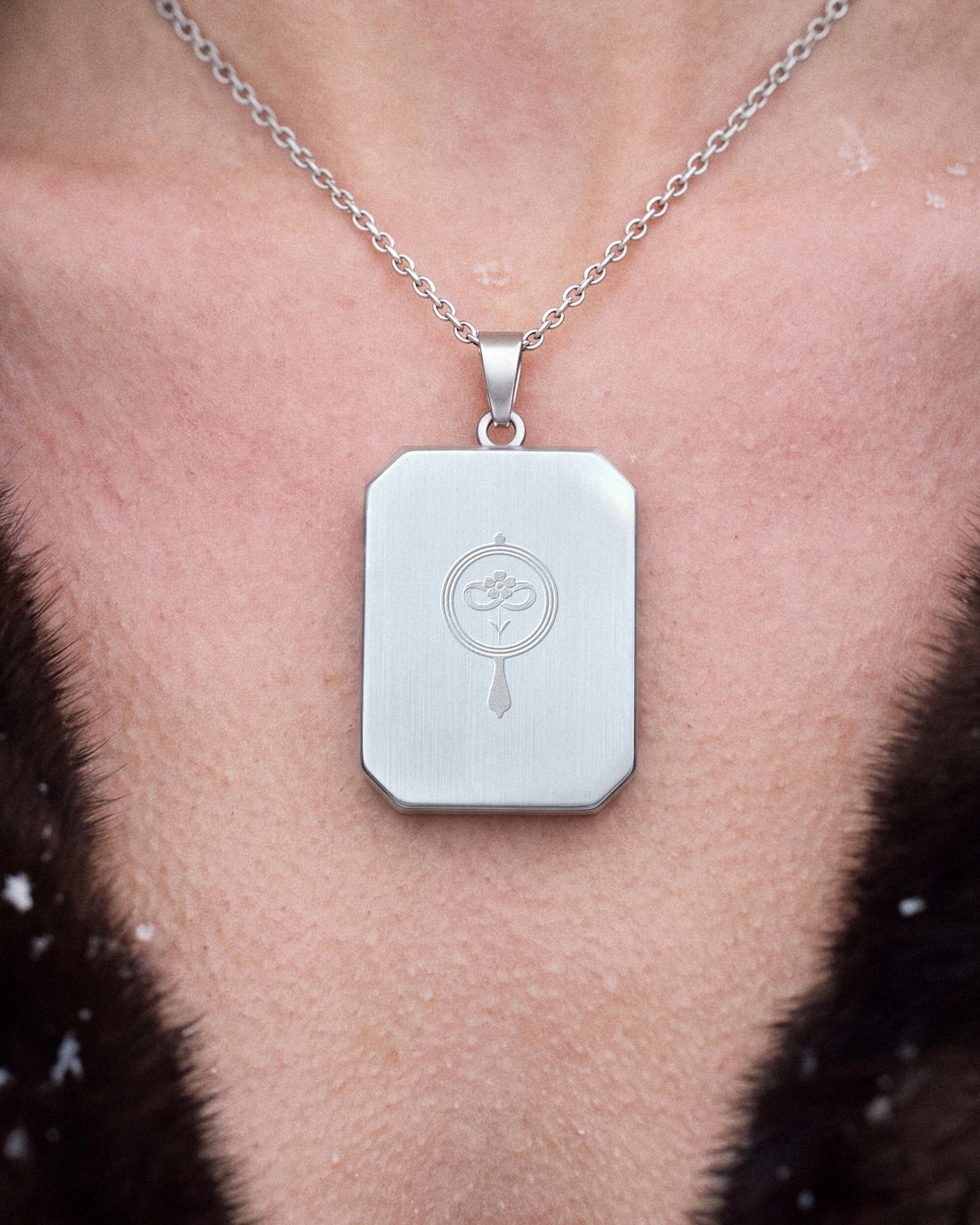 The Winter Between Us, the Amulet by Mirrors by Viulet, worn, close, turned to its back, the etched symbol of the Atelier