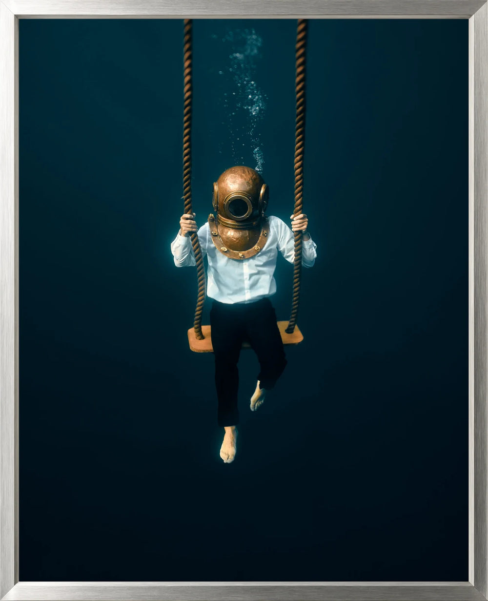 A figure wearing a diving helmet sits on a swing against a deep blue background, presented Lined in Midnight Silver